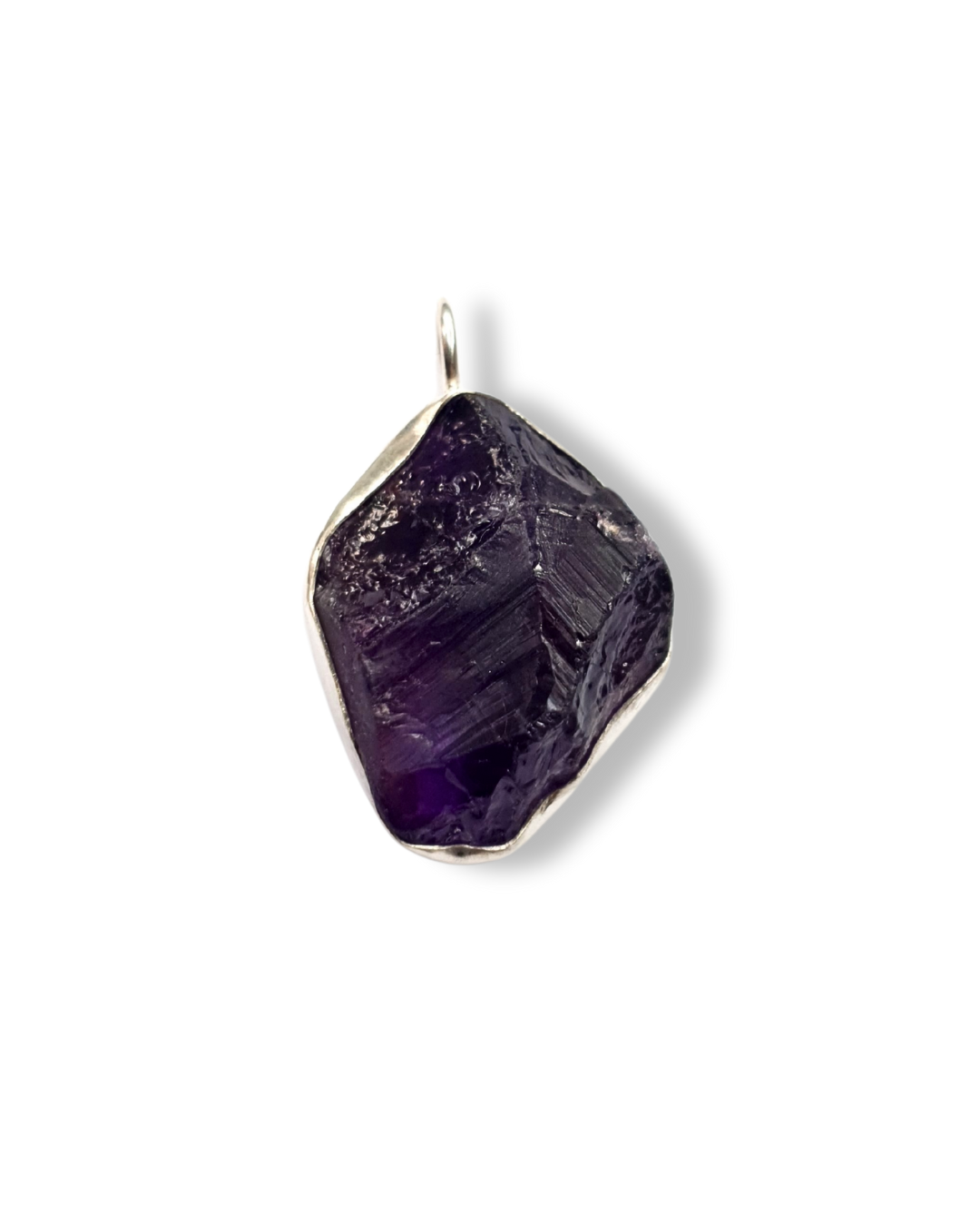 A rough-cut, irregular-shaped amethyst pendant in a silver bezel setting, with a rich and juicy purple color and rough, textured surface. The pendant is on a plain white background