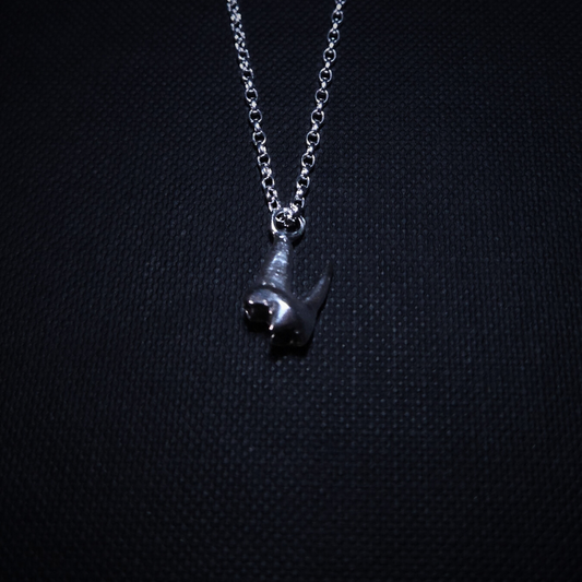 A tiny solid silver fox tooth hangs on a pendant against a black background