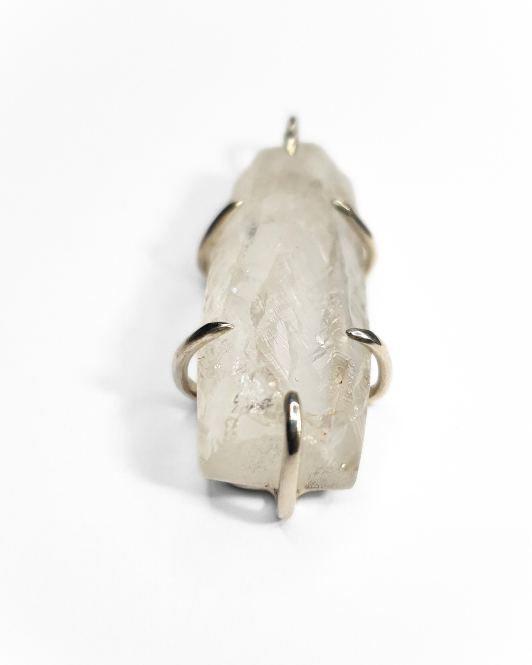 A rough-cut, semi-transparent, rectangular quartz pendant is photographed on a white background. The rough, beautifully textured stone is set in 6 silver claws - 1 and the top and bottom and two on each side.
