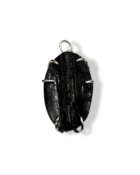 A rough-cut, oval-shaped black tourmaline is photographed from above on a white background. The rough, striated stone is set in 6 silver claws. spaced in 3 sets of two. A silver jump ring is visible at the top.