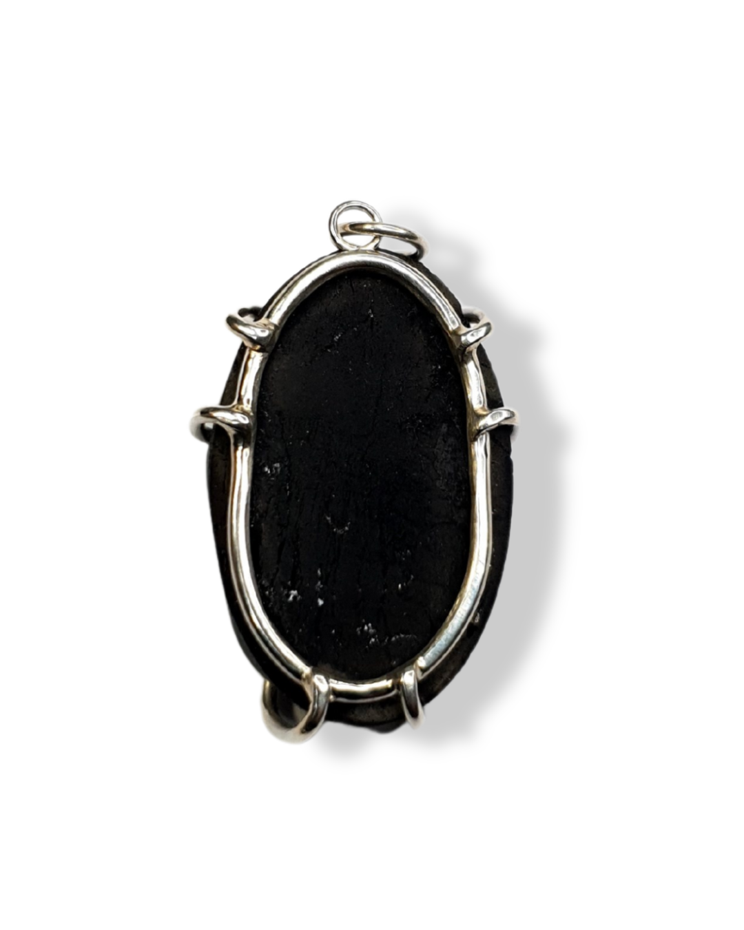 The back of black tourmaline and silver pendant is photographed on a white background. An oval-shaped silver frame sits against the smooth, flat back while 6 prongs come out from of the edges to hug the stone. There is a circular bail at the top which a jump ring is attached.