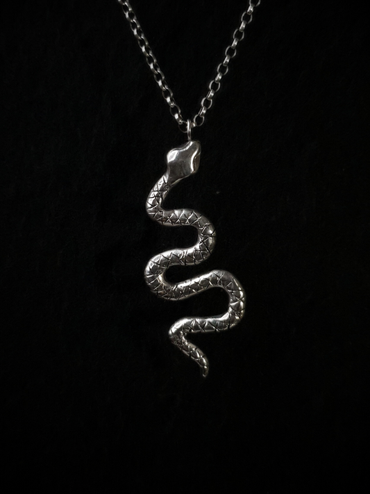 A large, solid sterling silver snake pendant hangs from a thick belcher chain on a black background. The snake is in a wavy position with its head at the top and the end of its tail at the bottom.