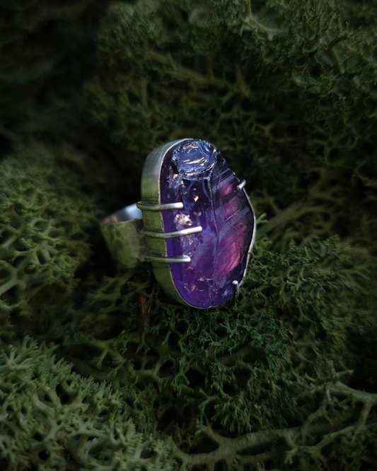 An androgynous style, rough-cut amethyst and sterling silver ring sits on a vibrant green bed of moss