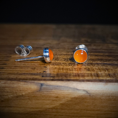 A pair of fiery orange carnelian & sterling silver round stud earrings on a wooden surface