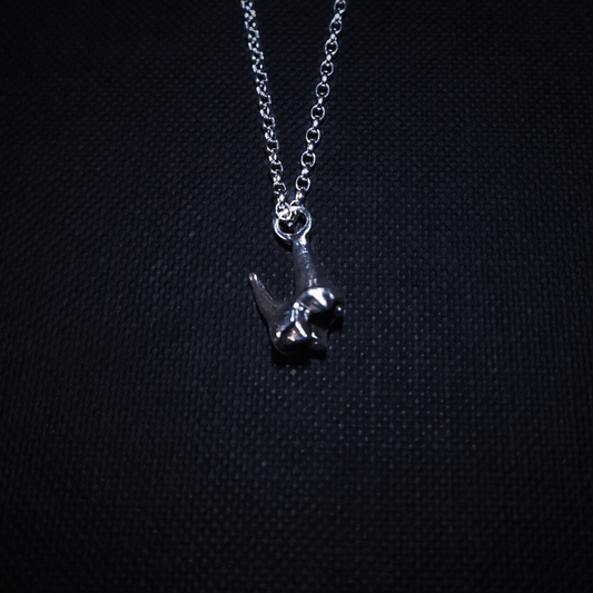 A tiny solid silver fox tooth hangs on a pendant against a black background