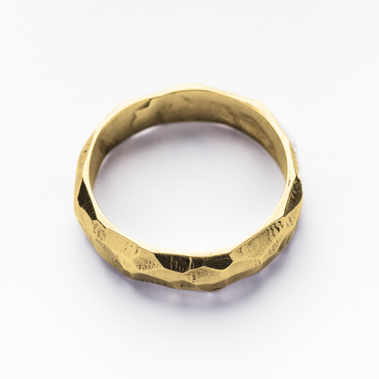 A 9ct yellow gold rough cut and faceted ring sits against a crisp, white background