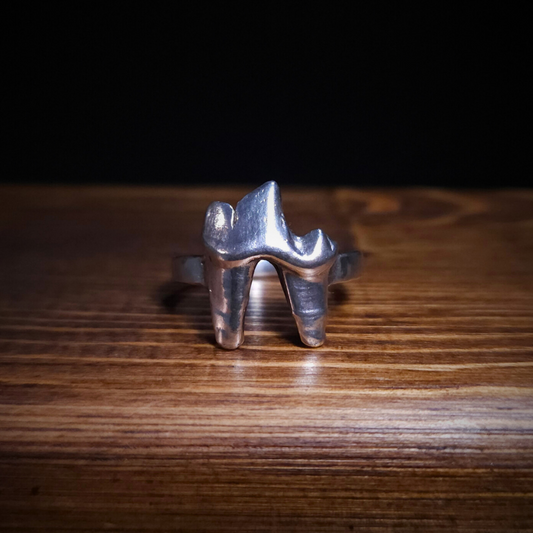 A sterling silver fox tooth ring sits on a wooden background.