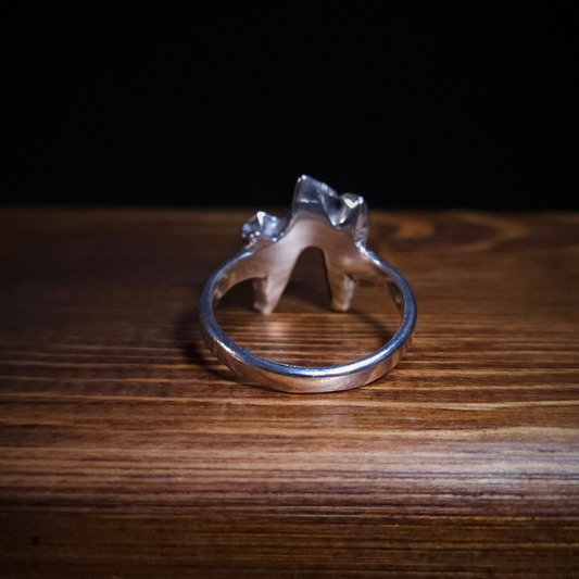 A sterling silver fox tooth ring is photographed sitting on a piece of wood. It is photographed from the back to show the smooth inside of the band.