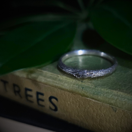 Sterling silver ring on a book titled 'TREES' with green leaves in the background.

The twig has deep longitudinal ridges and a knot in the centre. 