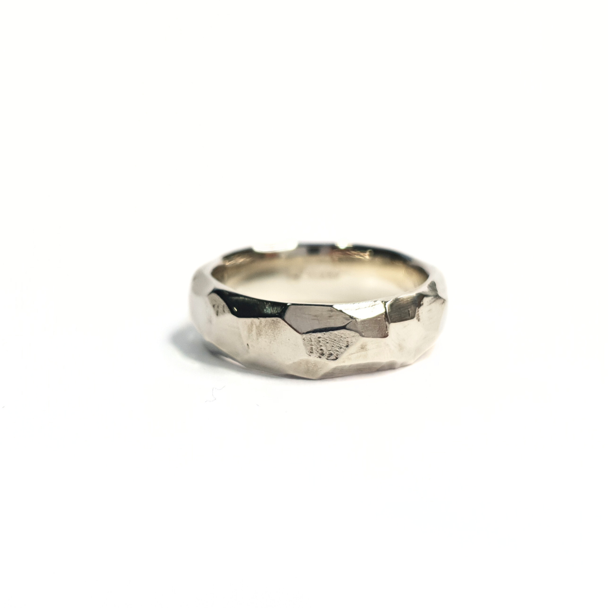 A 9ct white gold rough cut and faceted ring sits against a crisp, white background