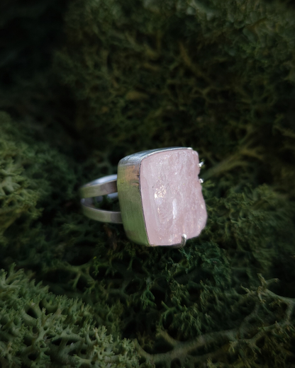 A pale-pink rose quartz and silver ring sits in a bed of moss. It has a split-style band and is oxidised with a satin finish.