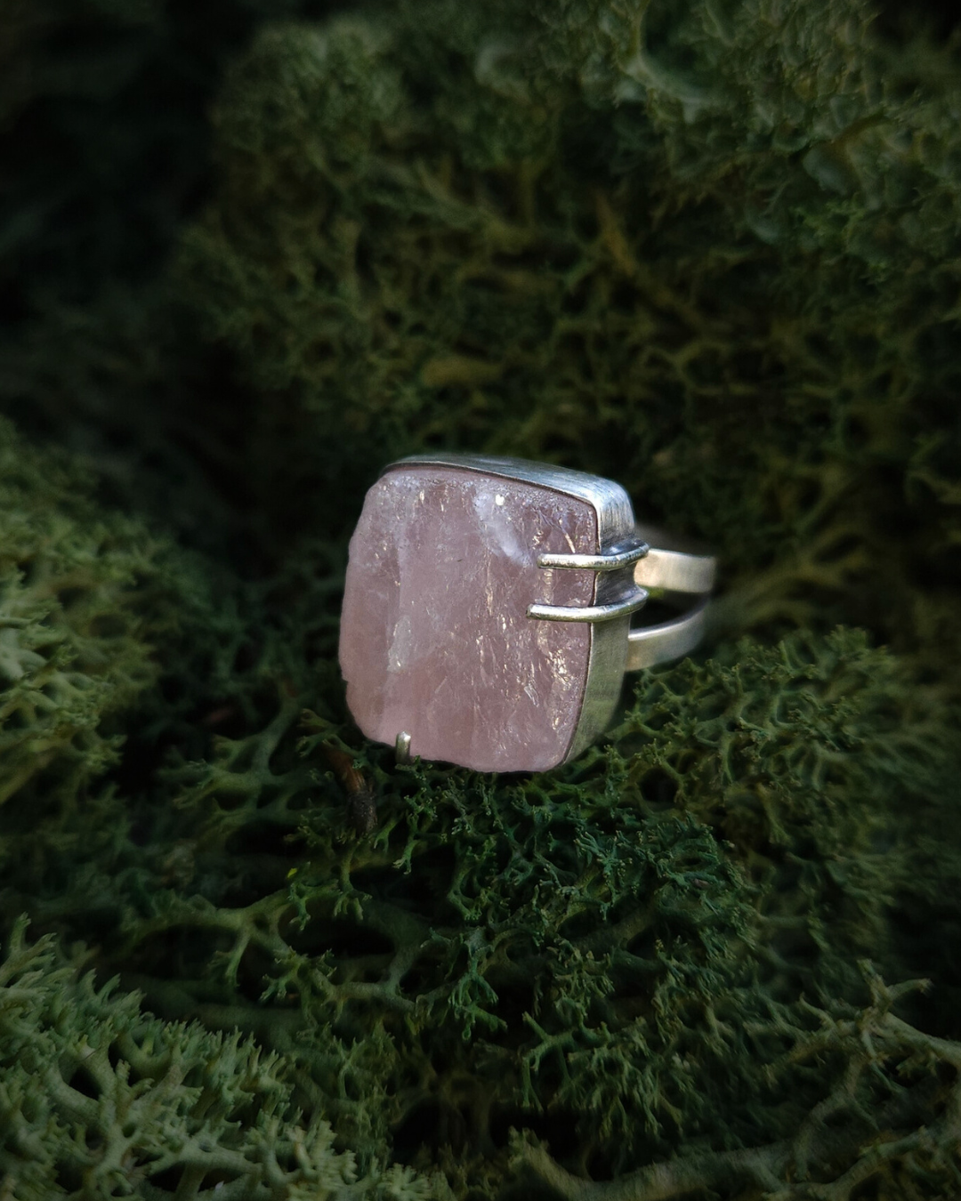 A square gothic androgynous rose quartz and sterling silver ring rest on a bed of green moss