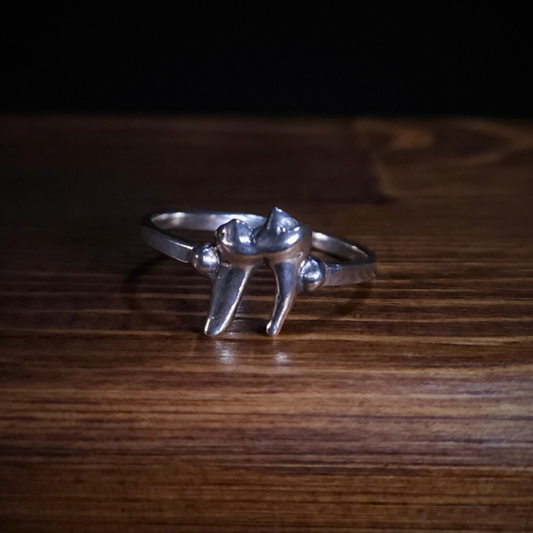 A sterling silver fox tooth ring sits on a wooden background.