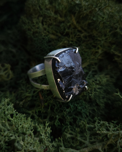 A Smoky Quartz rough cut stone ring rests in a bed of dark green moss. The ring is made from solid recycled sterling silver and has a split band. and claws. It has a gothic, alternative, androgynous style.