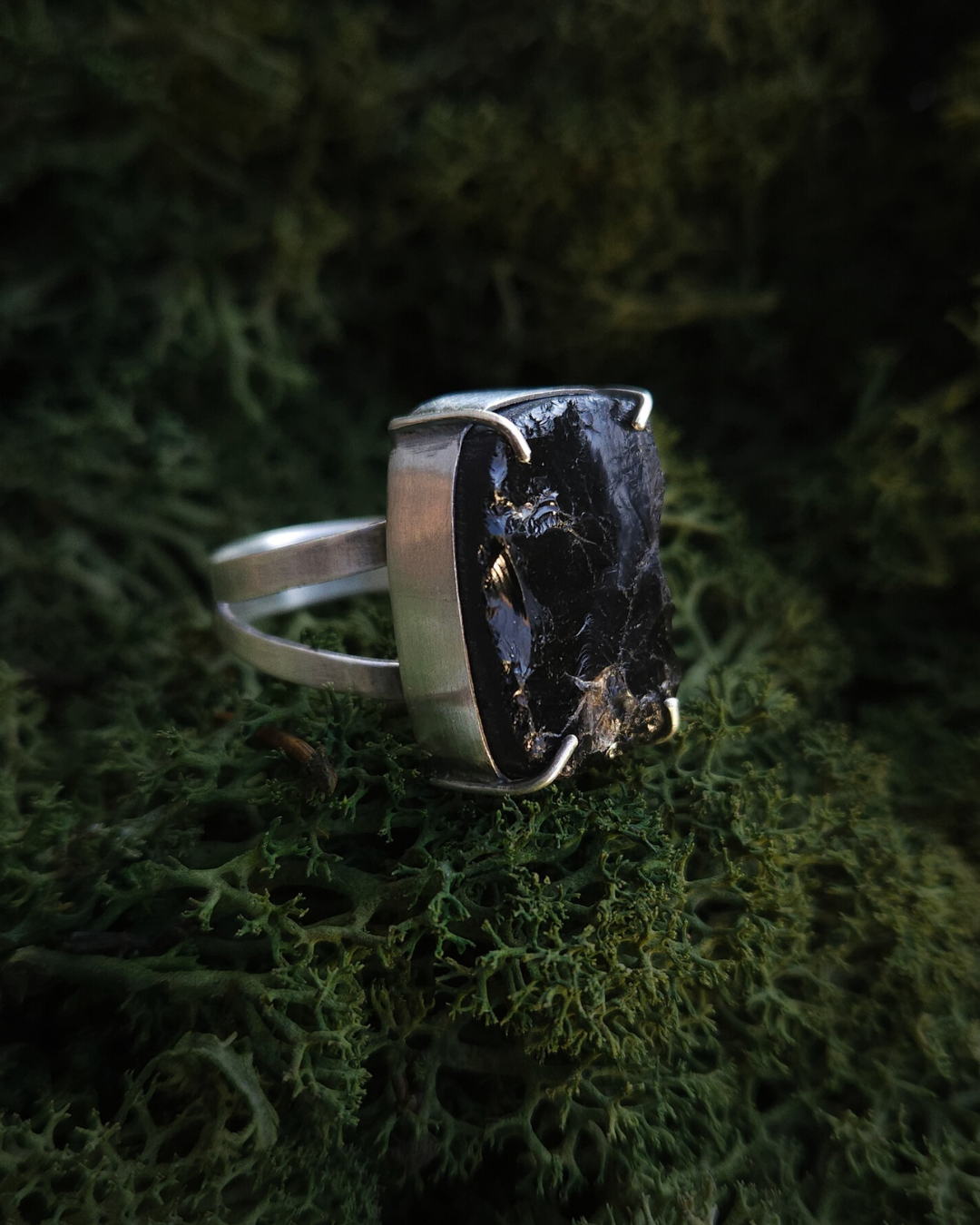 A rough cut Smoky Quartz gothic style ring rests in a bed of rich green moss. The ring is made from ethical recycled sterling silver and has a split band and claws. It has an alternative, androgynous style.