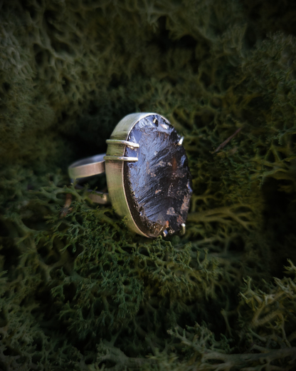 An oval shaped smoky quartz and ethical silver ring sit in a bed of green moss. It has a split-style band and claws. The surface of the stone is rough-cut, raw and covered in natural texture and craters.