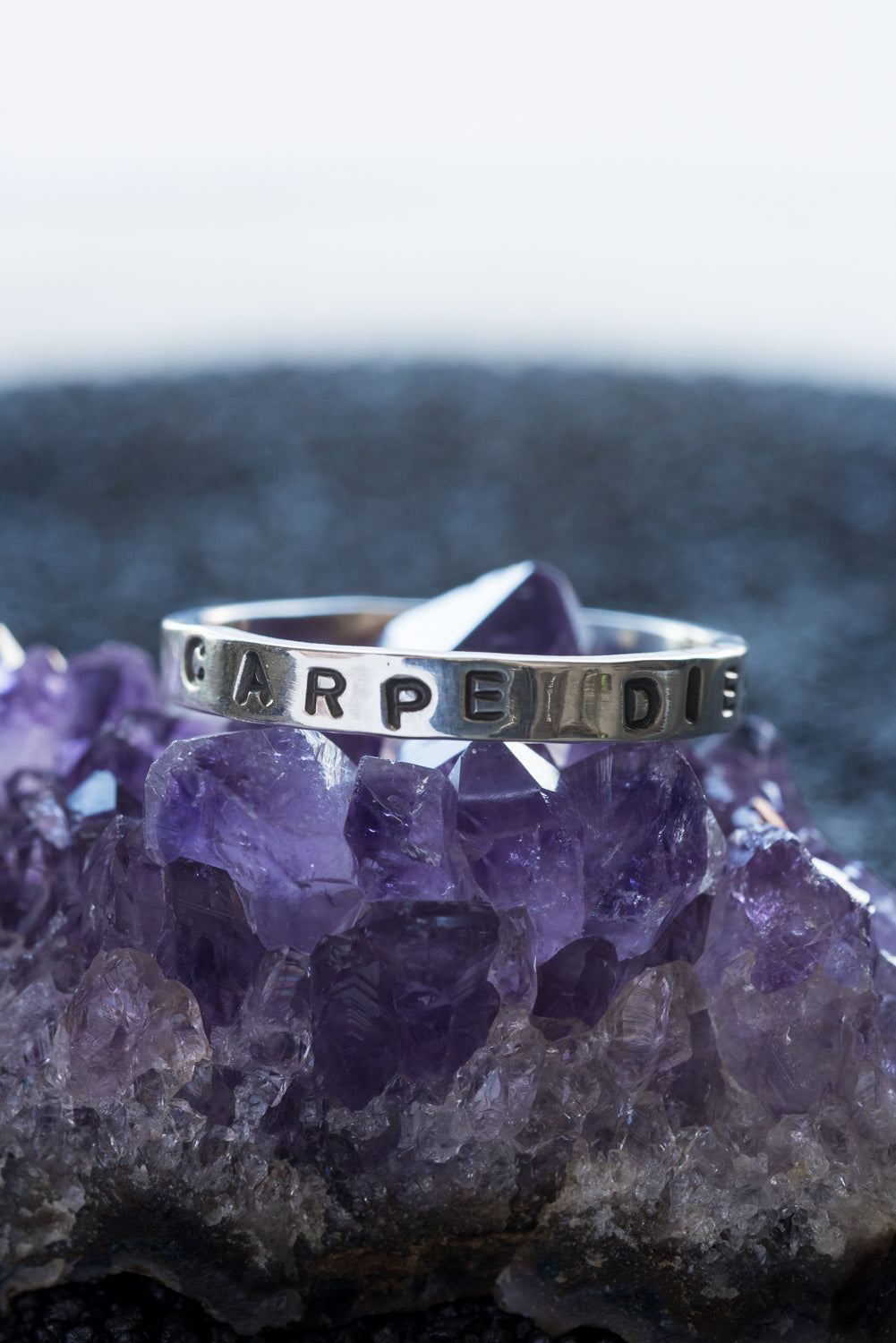 1 silver rings with the words "carpe diem" stamped into it,. It rests on a chunk of amethyst.