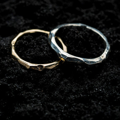 A 9ct gold ore ring and a silver ore ring sitting next each other on a black, sandy background.