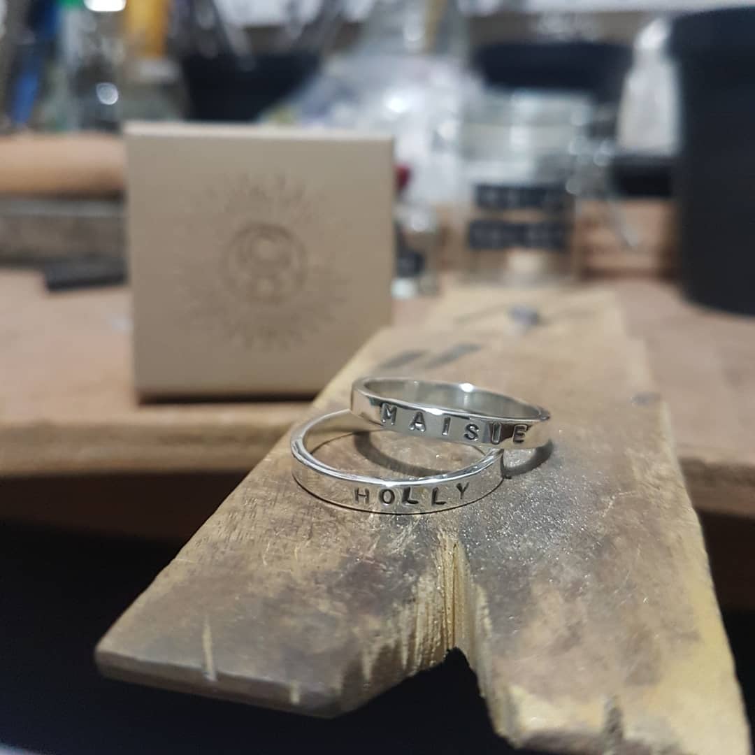 2 rings sit stacked on my workbench. The names "Maisie" and "Holly" are stamped on the outside of the rings.