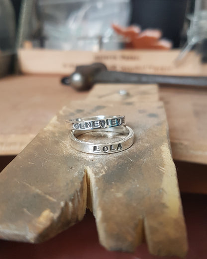 2 rings sit stacked on my workbench. The names "Genevieve" and "Lola" are stamped on the outside of the rings..