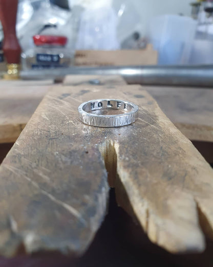 One ring sits on my workbench. The surname "Wolfe" is stamped inside. The outside of the ring has a hammered texture.