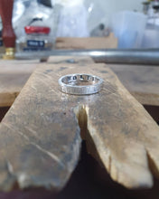 Load image into Gallery viewer, One ring sits on my workbench. The surname &quot;Wolfe&quot; is stamped inside. The outside of the ring has a hammered texture.
