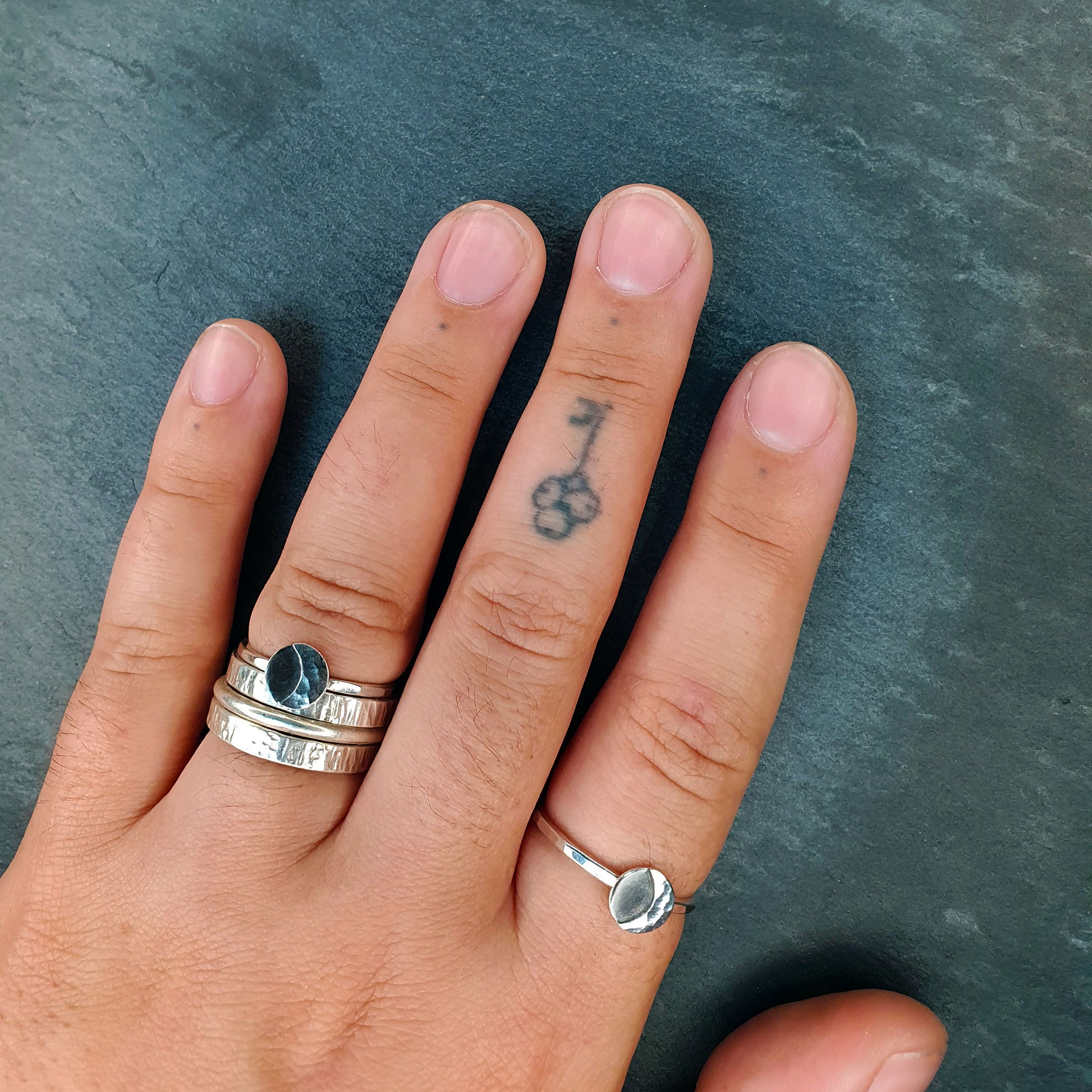 Riley wears one Luna ring stacked with his wedding bands and one alone on his forefinger. His nails are short and there's a small tattoo of a key on the last knuckle of his middle finger.