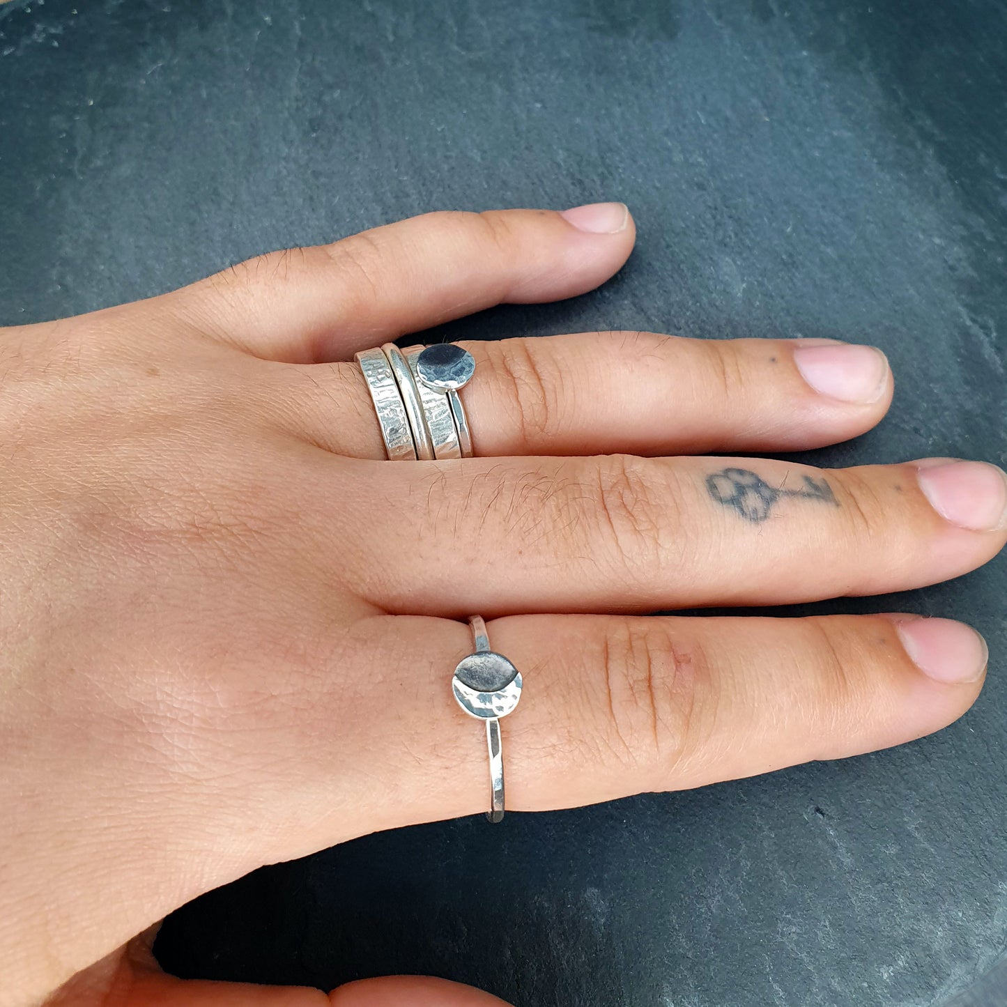 Riley wears one Luna ring stacked with his wedding bands and one alone on his forefinger. His nails are short and there's a small tattoo of a key on the last knuckle of his middle finger.