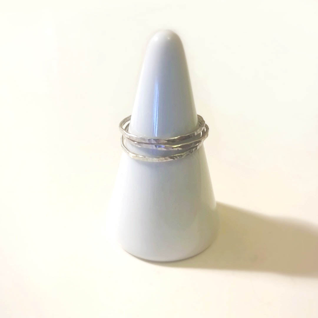 3 slim, silver stacking rings sit on a white ring cone.