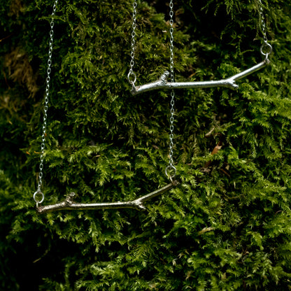 A Bronze and Silver Woodland necklace hang together against a green, mossy background
