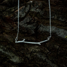 Load image into Gallery viewer, A silver woodland necklace on a dark, bark backgound
