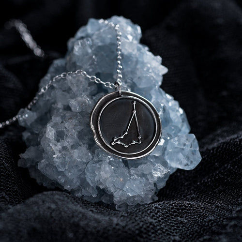 Capricorn zodiac necklace resting against a pale blue crystal on a black background