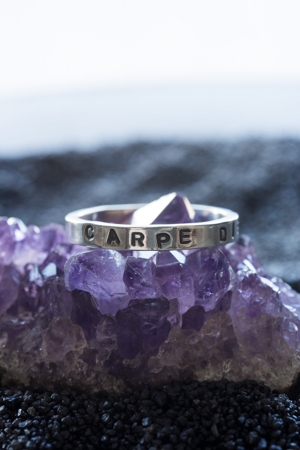 1 silver rings with the words "carpe diem" stamped into it,. It rests on a chunk of amethyst.