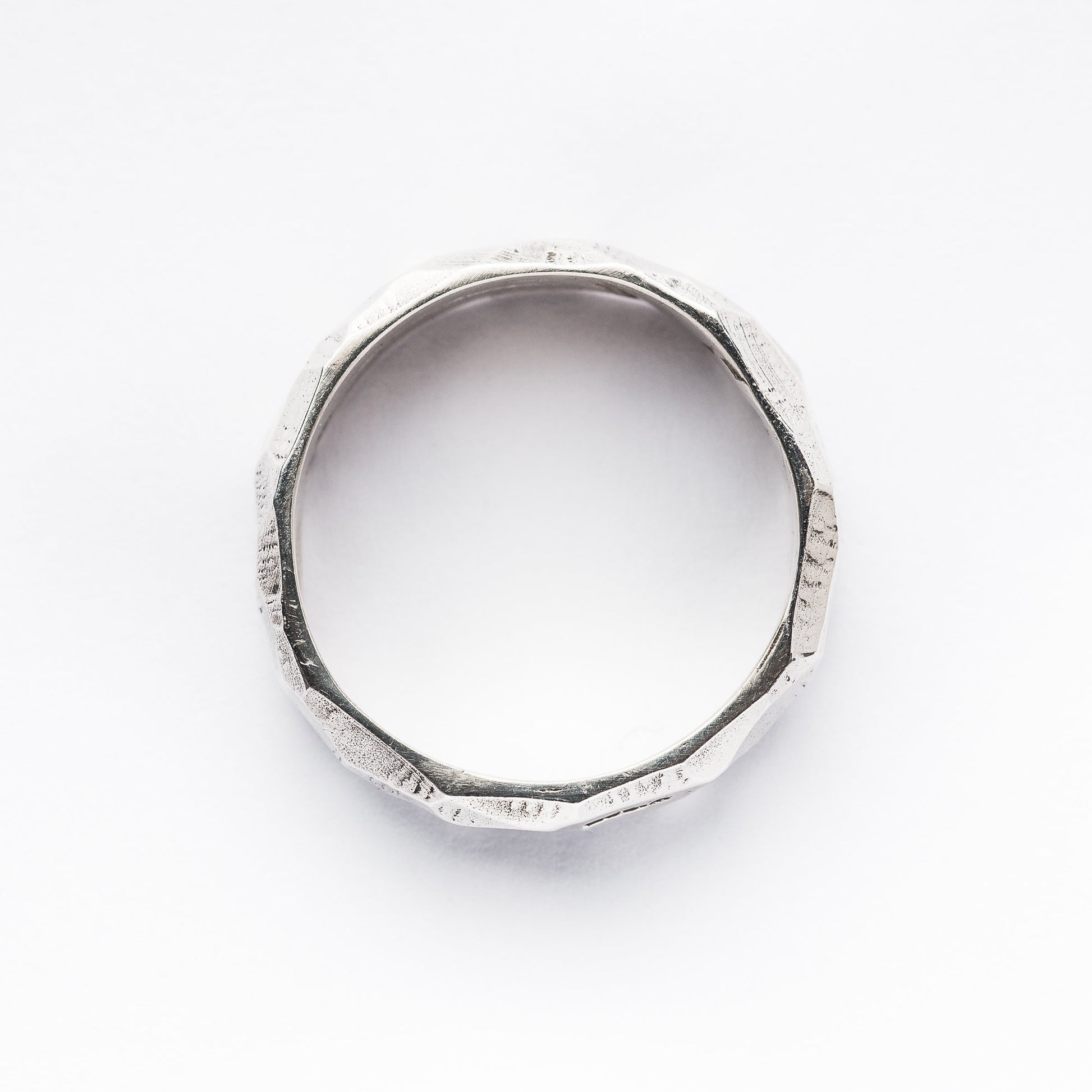 A silver rough cut and faceted ring sits against a crisp, white background. This view is from the top.
