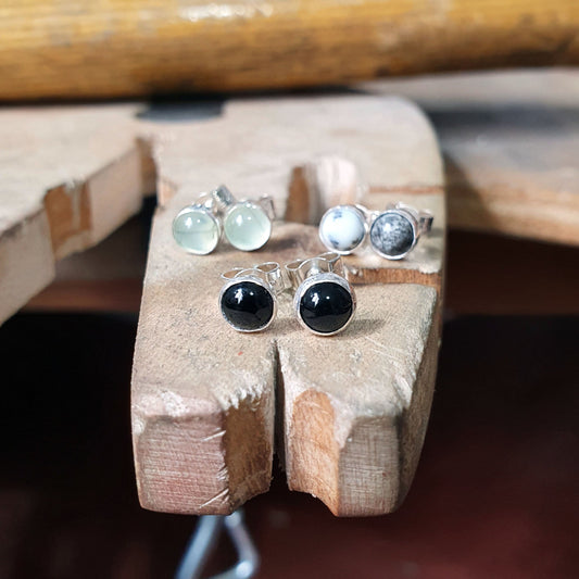3 pairs of gemstone and sterling silver stud earrings sit on a workbench with the black, onyx earrings in the foreground.